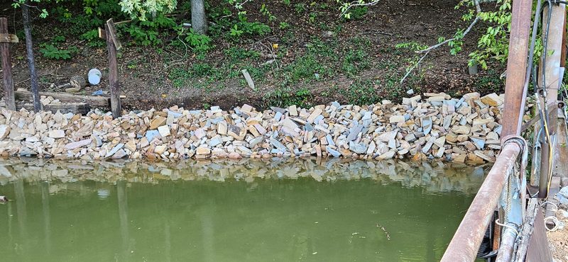 Stacked stone riprap along the water’s edge below a wooded lake bank
